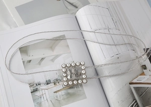 Close-up of square silver buckle with inlaid pearls on a thin beaded fashion chain belt