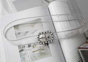 Detail of transparent PVC belt featuring pearl-encrusted square buckle and silver bead edges