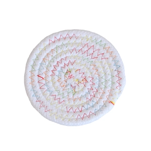 Close-up of circular white cotton rope woven coaster with colorful zigzag stitching detail