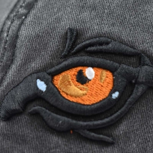 Macro detail of high-quality embroidery of eyes on dark grey washed cotton baseball cap