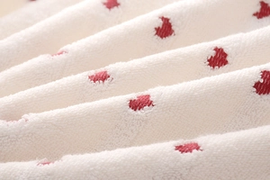 Close-up of white cotton terry towel featuring detailed red heart pattern embroidery