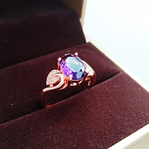 Macro shot of rose gold ring with oval purple gemstone in brown velvet jewelry box