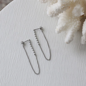 Detailed view of silver minimalist long chain tassel earrings on a white textured stand