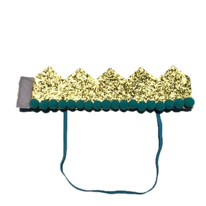 Detail of a gold sequin party crown with green pom-poms and adjustable elastic strap