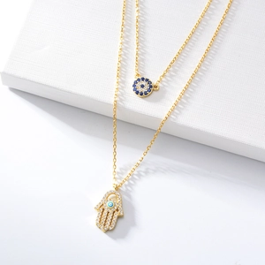 Detailed shot of double-layer gold Hamsa Hand and Evil Eye pendants with sparkling zircons