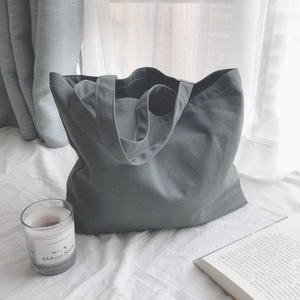Grand sac cabas en toile grise minimaliste avec doubles anses sur un lit blanc épuré
