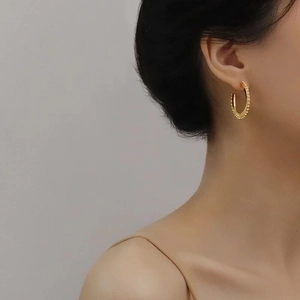 Minimalist matte gold geometric C-hoop earrings with beaded edges worn by a model