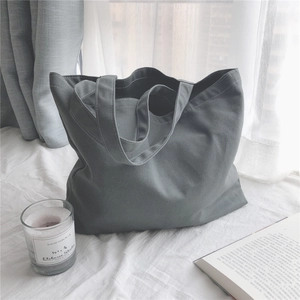 Gros plan d'un sac cabas en toile grise avec anses solides sur fond de literie blanche