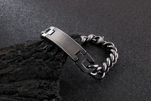 Detail of dark grey gunmetal Cuban link bracelet with rectangle plate on black rock