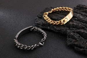Close-up of gold and gunmetal stainless steel curb chain bracelets on a textured background