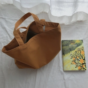 Détail d'un sac cabas en toile caramel avec de larges bretelles sur un lit blanc