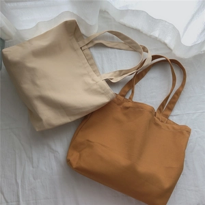 Gros plan de sacs cabas en toile crème et caramel sur une literie blanche douce