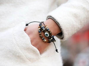Detail of beaded leather bracelet with blue evil eye charm worn on wrist with furry coat