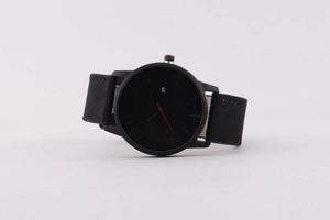 Détail de la montre minimaliste noire avec trotteuse rouge et affichage du calendrier