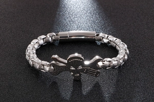 Detailed close-up of a silver skull and wrench charm on a heavy metal curb chain bracelet