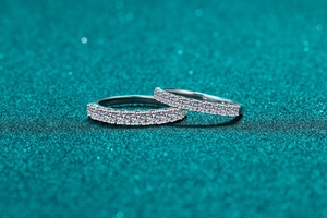 Macro shot of two silver-tone eternity rings with round-cut pavé diamonds on teal background