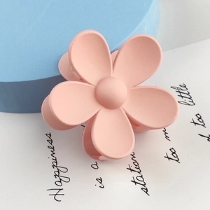 Detail view of a large matte pink flower hair claw clip on a decorative background