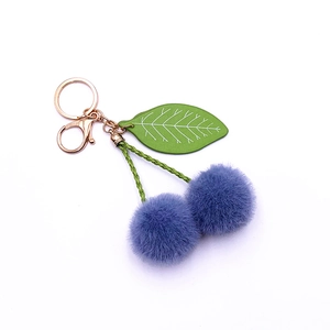 Cute plush cherry keychain with purple pom poms, green woven stems and gold metal clasp