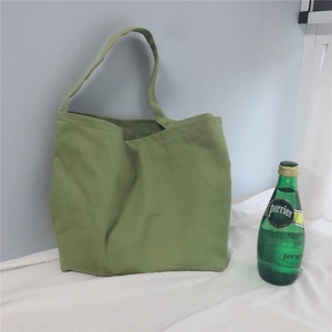 Detail of green canvas tote bag with long shoulder strap in a minimalist indoor setting