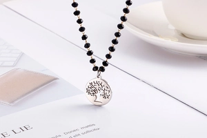 Detailed flat lay of black beaded necklace featuring a silver tree of life pendant