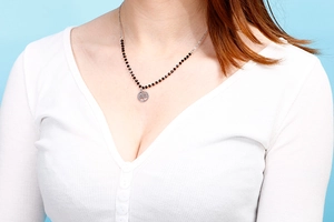 Detail of silver chain necklace with black beads and Tree of Life pendant on a model