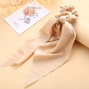 Detail of champagne satin scrunchie with long ribbons on a minimalist display stand