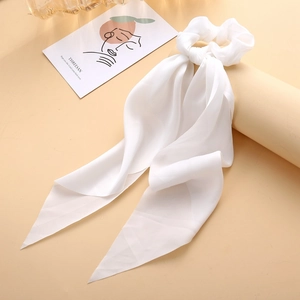 Detail of white satin bow hair tie scrunchie with long ribbons on soft beige background