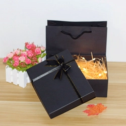 Detail of elegant black gift box with gold-edged ribbon bow and warm LED fairy lights inside