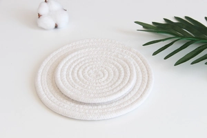 Detail view of woven white cotton rope coasters with natural texture and green leaf decor