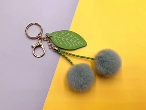 Detailed view of plush cherry keychain with soft blue pompoms and golden metal ring