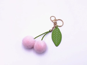 Close-up of pink faux fur cherry keychain with green woven rope and gold metal clasp