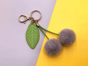 Detail of plush cherry keychain with gray pom-poms, green leaf, and golden lobster clasp