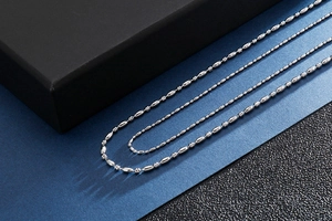 Detail view of two silver stainless steel beaded necklaces on a textured dark background