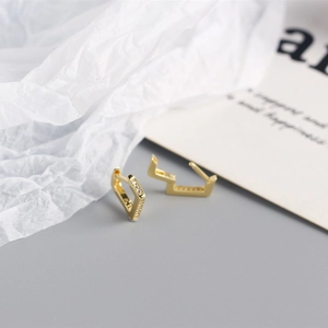 Detail showing polished gold geometric earrings with white zircon stones on creative props
