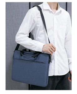 Blaue Laptoptasche aus Stoff mit schwarzen Griffen und Gurt, von Modell getragen