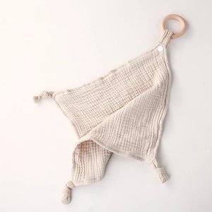 Detail of beige cotton muslin baby comforter with natural wood teething ring and knots