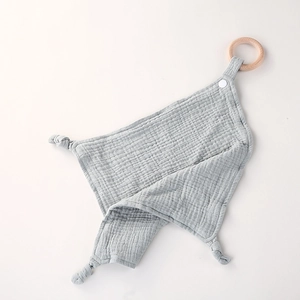 Macro shot of grey cotton muslin baby security blanket with a natural wooden teething ring