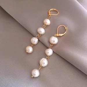 Elegant gold earrings with white baroque freshwater pearls on grey silk fabric backdrop