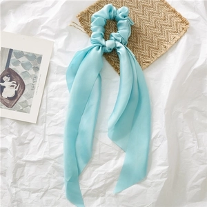 Close-up of light blue satin scrunchie with long ribbons on a minimalist aesthetic background