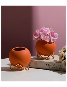 Macro detail of terracotta ceramic ball vase with a golden triangular wire stand