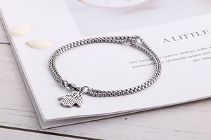 Macro detail of silver Hamsa Hand charm on stainless steel chain over floral background