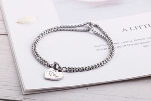 Close-up of a silver box chain bracelet with Love engraved heart pendant on wood surface