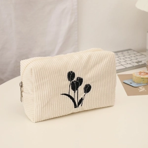 Detail view of corduroy makeup bag featuring floral embroidery and metal zipper closure