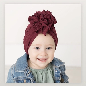 Detail of burgundy ribbed cotton baby turban hat with a large wavy fabric flower