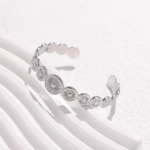 Detail shot of silver geometric open cuff with sunburst embossed patterns on white surface