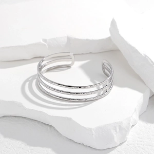 Close-up of triple-layered silver stainless steel open bangle on white stone props