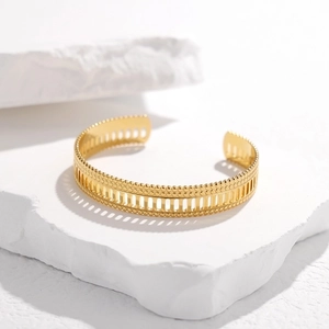 Detailed close-up of golden hollow geometric cuff bracelet on minimalist stone display