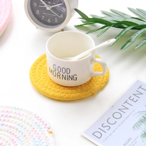 Detail of yellow woven cotton coaster with white ceramic mug and spoon in a lifestyle setting