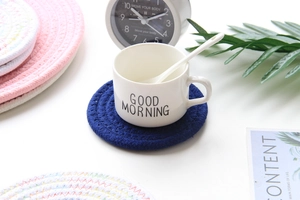 Detail view of a navy blue woven cotton coaster featuring a white mug in a home setting