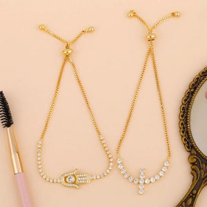Detail of gold crystal bracelets with Hamsa and Cross charms featuring adjustable drawstrings